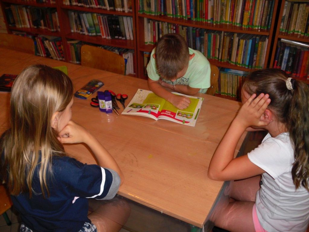 uczestnicy bibliotecznych zajęć słuchają dzisiejszej opowieści czytanej przez jednego z chłopców
