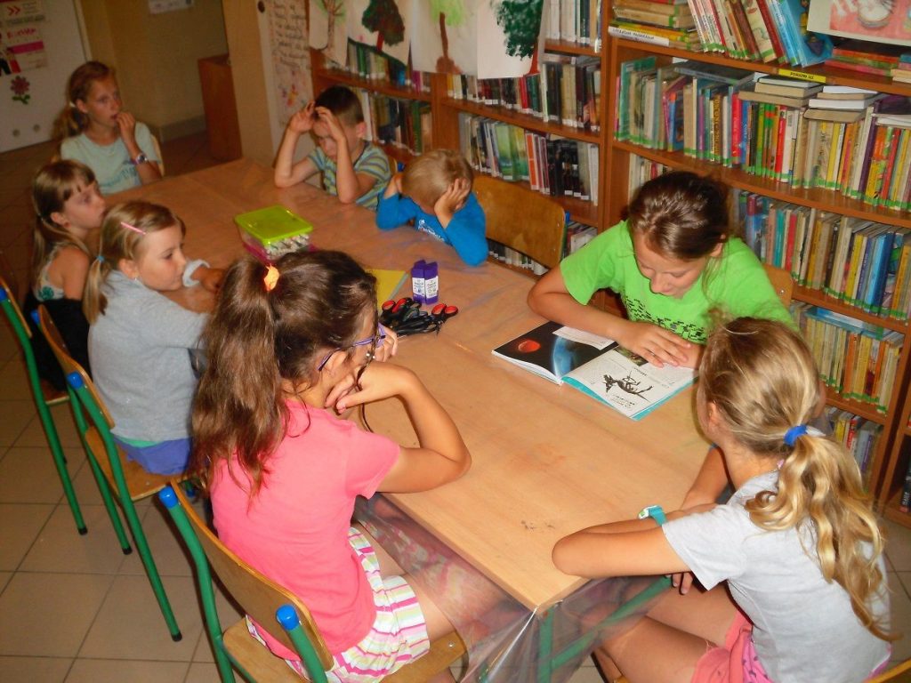 uczestnicy wakacyjnych zajęć w bibliotece słuchają dalszej części opowiadania czytanej przez kolejną z dziewczynek