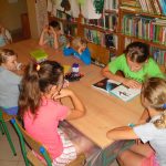 uczestnicy wakacyjnych zajęć w bibliotece słuchają dalszej części opowiadania czytanej przez kolejną z dziewczynek