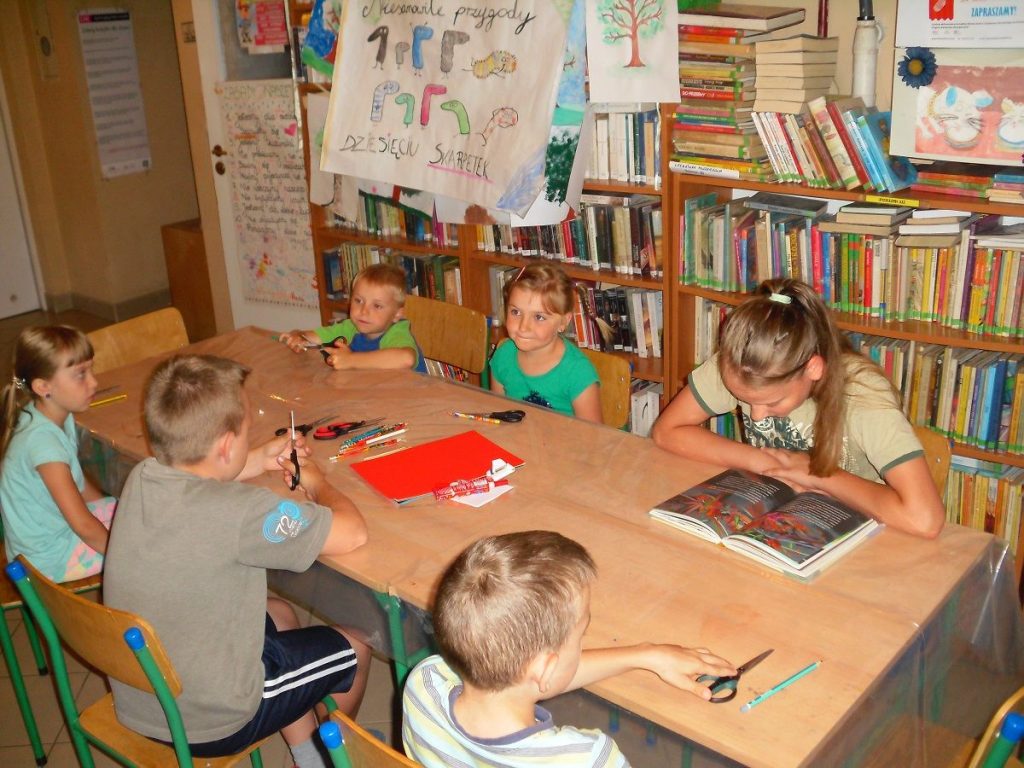 dzieci uczestniczące w wakacyjnych zajęciach z uwagą słuchają opowieści o  skarpetce czytanej przez jedną z dziewczynek