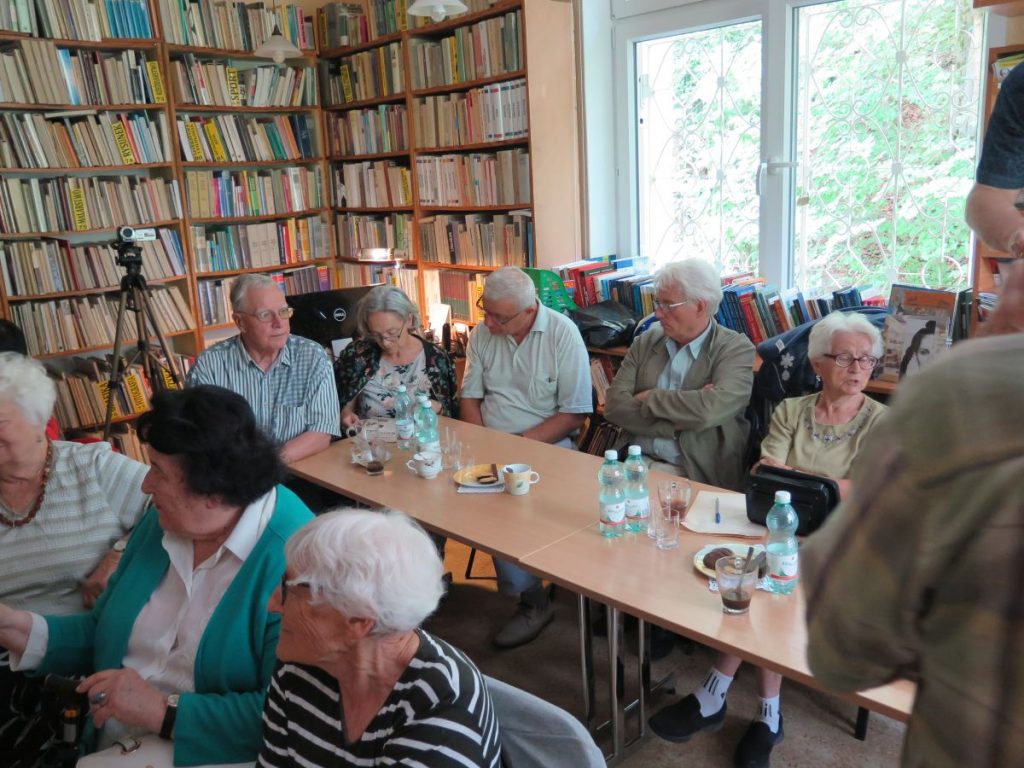 Licznie zgromadzeni w czytelni Biblioteki Publicznej goście siedzą przy stolikach i oczekują na projekcję przedwojennego filmu o Krynicy