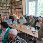 Licznie zgromadzeni w czytelni Biblioteki Publicznej goście siedzą przy stolikach i oczekują na projekcję przedwojennego filmu o Krynicy
