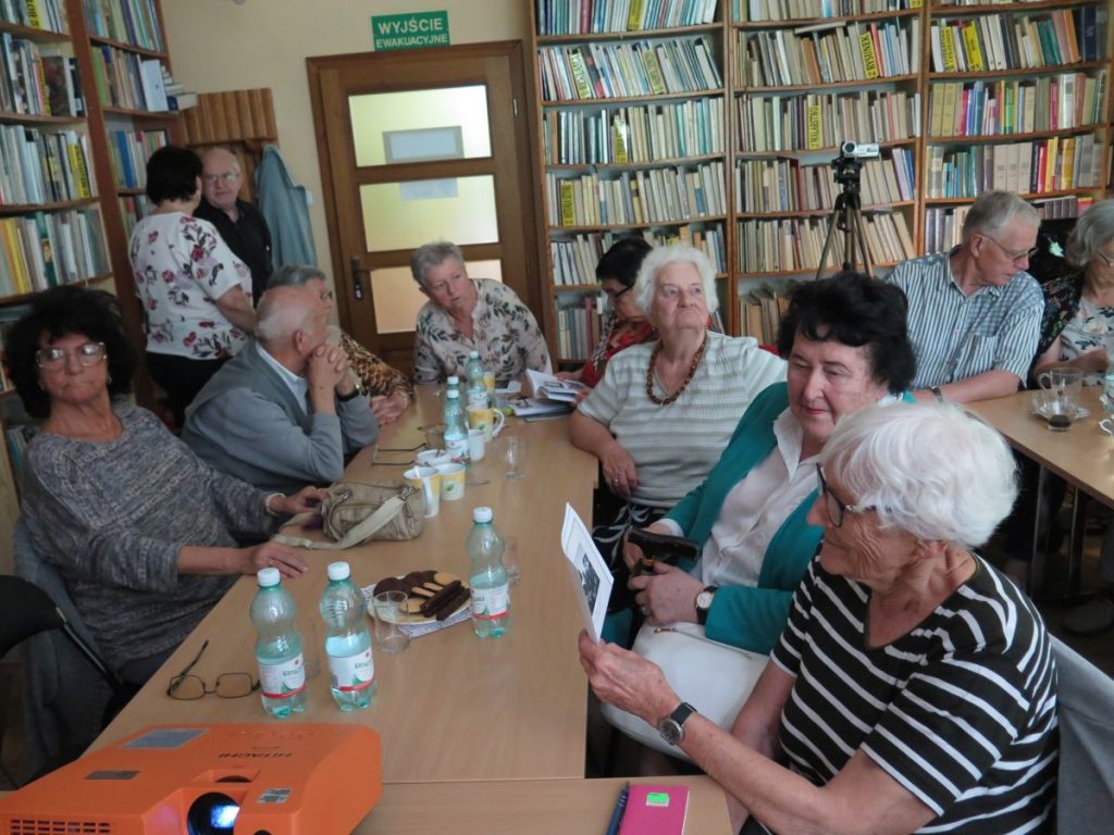 Licznie zgromadzeni w czytelni Biblioteki Publicznej goście siedzą przy stolikach i oczekują na projekcję przedwojennego filmu o Krynicy