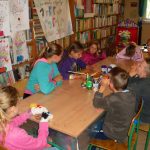 dzieci podczas wakacyjnych zajęć w Bibliotece z uwagą słuchają opowieści czytanej przez jedną z dziewczynek