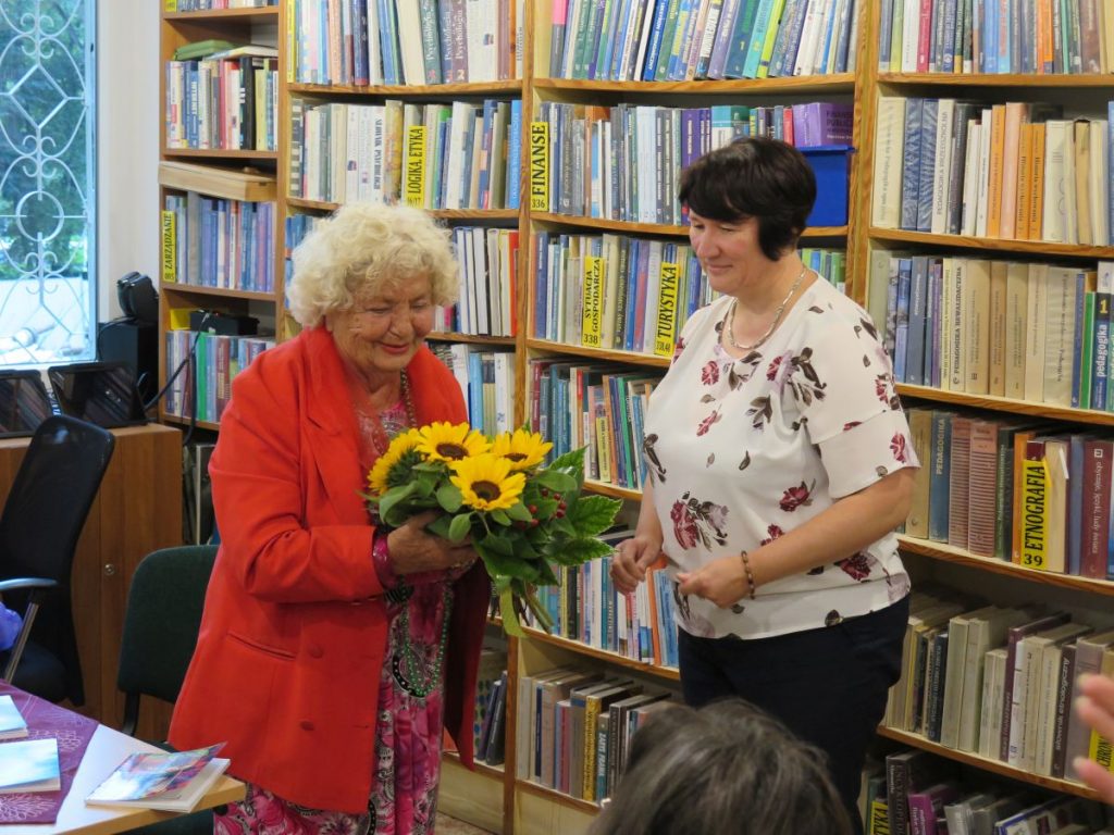 Dyrektor Biblioteki Publicznej Pani Magdalena Krzeszowska wręcza uśmiechniętej Felicji Borzyszkowskiej- Sękowskiej bukiet pięknych żółto- zielonych kwiatów
