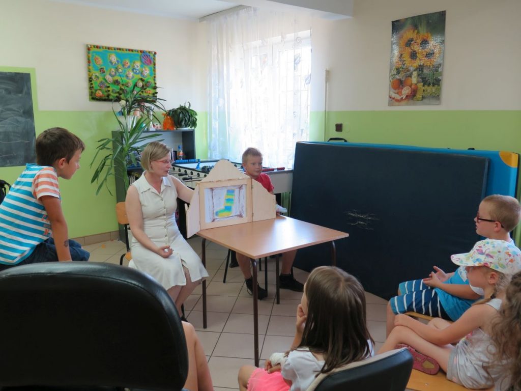 Pani Bibliotekarka razem z jednym z chłopców rozkłada na stoliku teatrzyk kamishibai