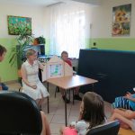 Pani Bibliotekarka razem z jednym z chłopców rozkłada na stoliku teatrzyk kamishibai