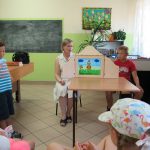 Pani Bibliotekarka razem z jednym z chłopców rozkłada na stoliku teatrzyk kamishibai