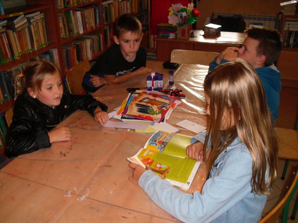 Dzieci w czasie zajęć w bibliotece z uwagą słuchają opowieści czytanej przez jedną z dziewczynek