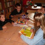 Dzieci w czasie zajęć w bibliotece z uwagą słuchają opowieści czytanej przez jedną z dziewczynek