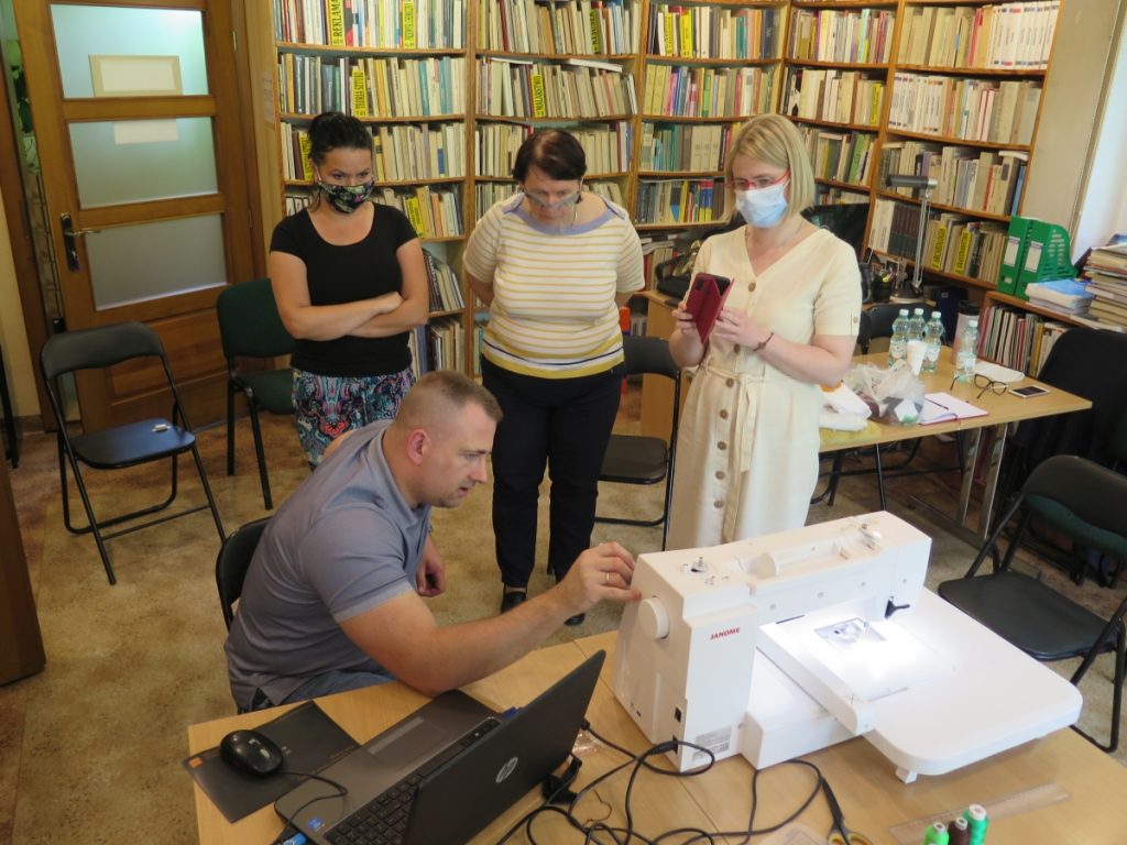 Na zdjęciu mężczyzna tłumaczy zasady działania hafciarki trzem kobietom które pracują w bibliotece