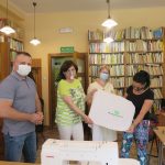 Na zdjęciu stoi 1 mężczyzna, który prowadził szkolenie z obsługi hafciarki oraz uczestniczki 3 kobiety. Pokazują wyhaftowane na materiale logo biblioteki.