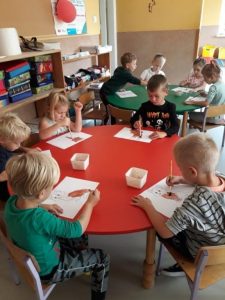Dzieci siedzą przy stolikach i kolorują wcześniej przygotowane rysunki