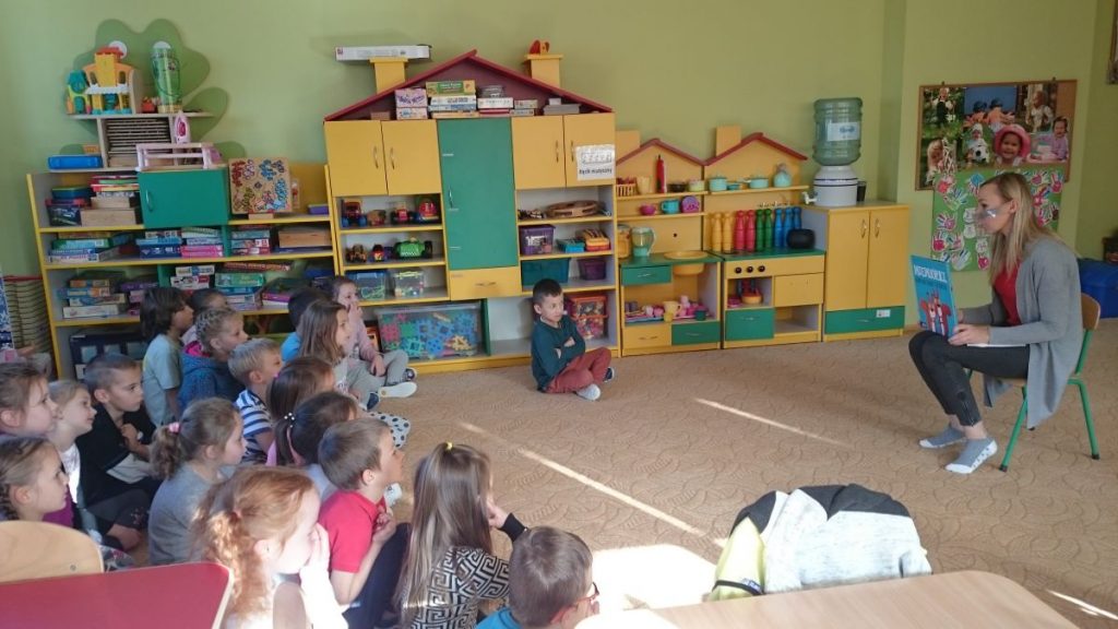 Grupa przedszkolaków słucha czytanej przez bibliotekarza bajki