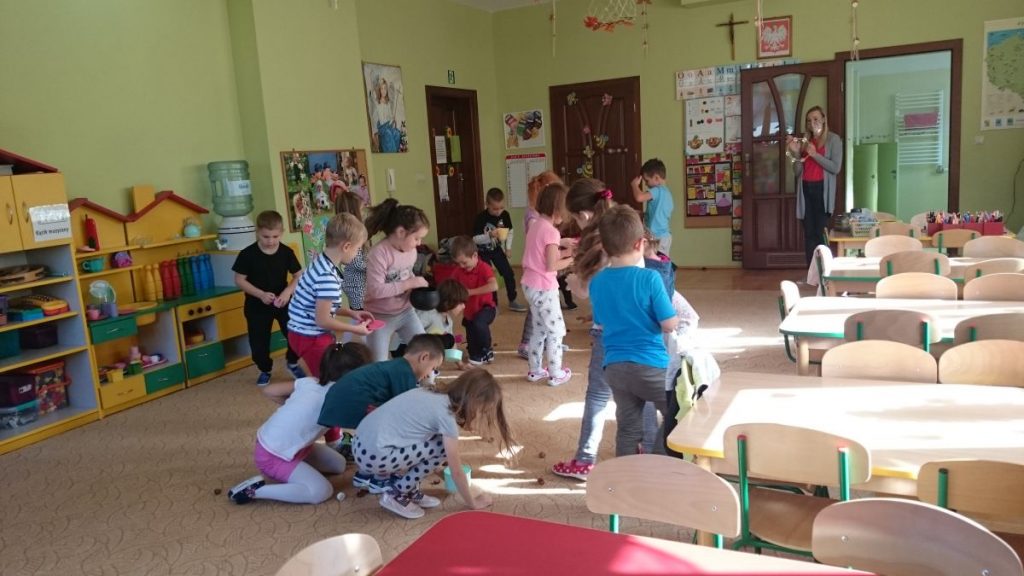 Grupa przedszkolaków bierze udział w zabawie ruchowej pt. "Orzechobranie" polegającej na tym, że przedszkolaki wcielają się w role wiewiórek i gromadzą zapasy na zimę w postaci szyszek, orzechów, kasztanów.