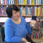 Na krześle siedzi pani dyrektor biblioteki Magdalena Krzeszowska trzyma w reku głowę manekina, który na głowie ma kapelusz.