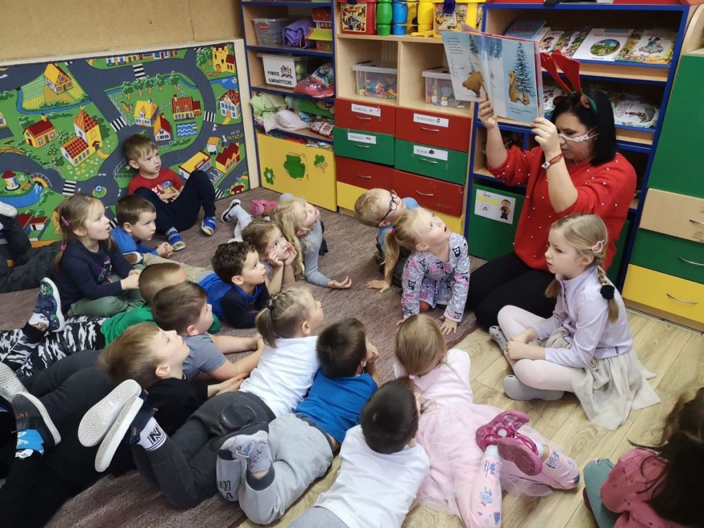 Dzieci wraz z paną siedzą zn podłodze. Oglądają bajkę. którą pani bibliotekarka pokazuje.