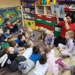 Dzieci wraz z paną siedzą zn podłodze. Oglądają bajkę. którą pani bibliotekarka pokazuje.