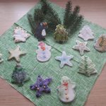 Na zdjęciu figurki wykonane z masy porcelanowej gwiazdki, mikołaj,choinka, aniołek. Połozone na zielonej serwetce wraz z zielonymi gałązkami .