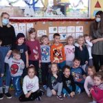Na zdjęciu część dzieci stoi, część siedzi na podłodze. Obok dzieci stoją dwie panie z przedszkola i dwie panie z biblioteki. Wszyscy stoją w sali przedszkola do wspólnego zdjęcia.