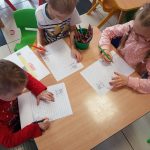 Jedna dziewczynka i dwóch chłopców siedzą przy stoliku i wykonują prace plastyczne