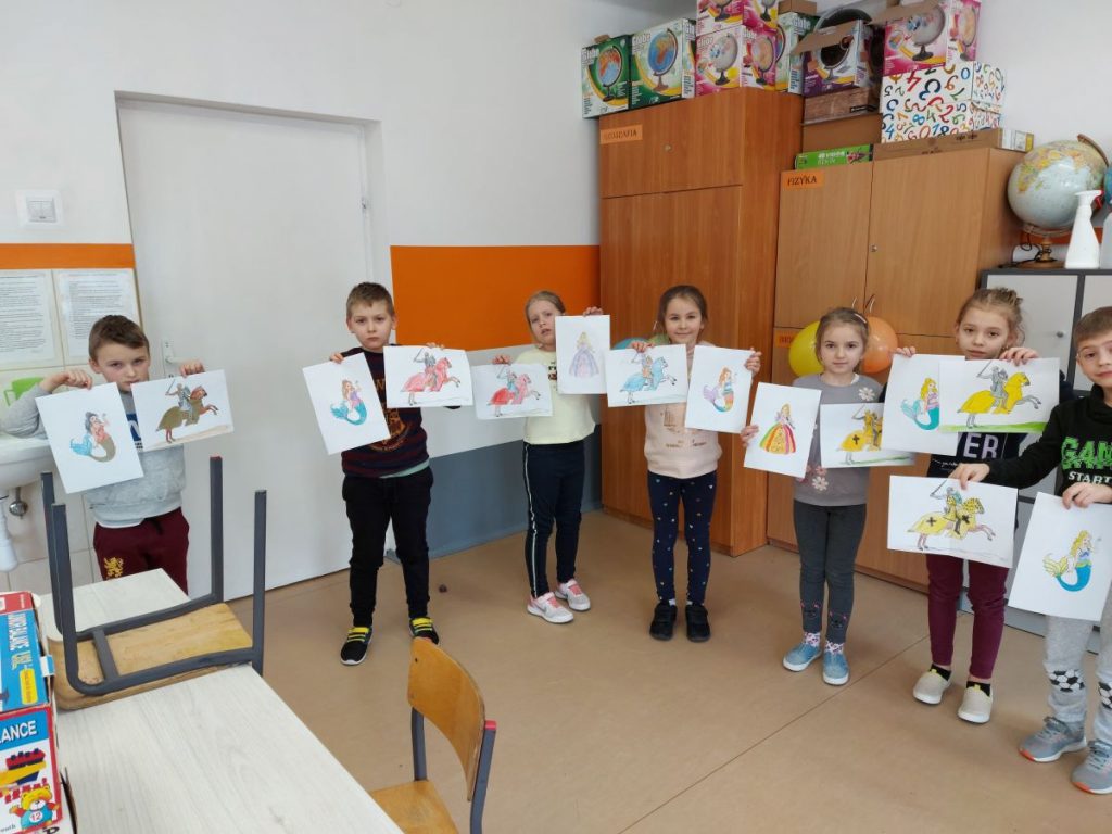 Grupa dzieci stoi w sali i trzyma w ręku prace wykonane przez siebie