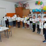 Grupa dzieci stoi w sali i trzyma w ręku prace wykonane przez siebie