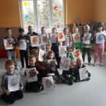 Liczna grupa przedszkolaków pozuje wspólnie do pamiątkowego zdjęcia, wszyscy trzymają w rękach swoje piękne rysunki