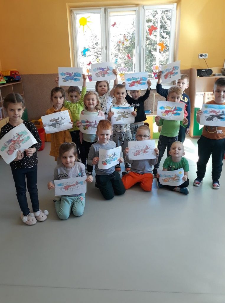 Na środku sali ustawiła się uśmiechnięta grupa przedszkolaków, każde trzyma w rękach narysowaną przed momentem wspaniałą podniebną maszynę