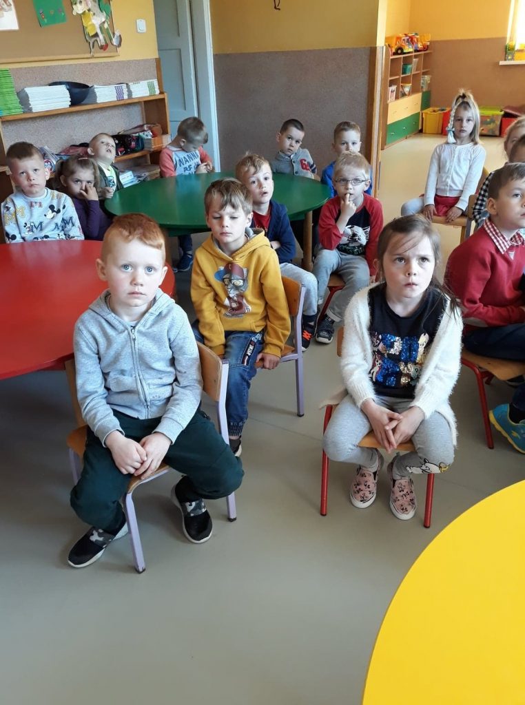 W sali przedszkolnej grupa dzieci siedzi na krzesełkach i słucha bajki pt. „Jak mama została Indianką”.