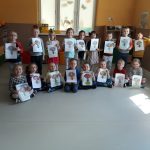 Grupa przedszkolaków ustawiła się do grupowego zdjęcia, każde z dzieci trzyma w rączkach namalowany przed momentem piękny rysunek.
