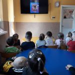 W sali przedszkolnej grupa dzieci słucha czytanej im przez Pana Borsuka bajki o śmiesznym Scooby-Doo