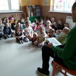 Dzieci siedzą w przedszkolnej sali i słuchają w skupieniu historii o Franklinie piłkarzu, którą czyta im pan bibliotekarz