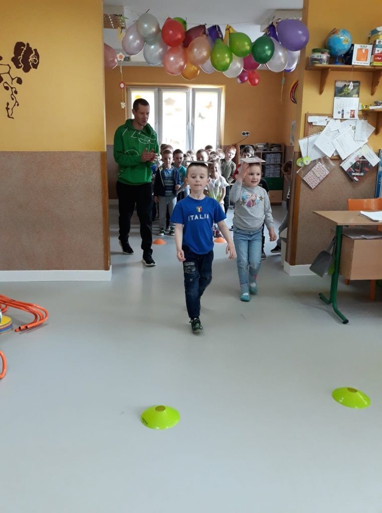 Dwóch chłopców idzie wyprostowanych i skoncentrowanych, a na ich głowach leżą małe książki. Zawodnicy muszą przejść wyznaczoną trasę, uważać żeby nie spadła im książka i wrócić jak najszybciej do swoich drużyn.