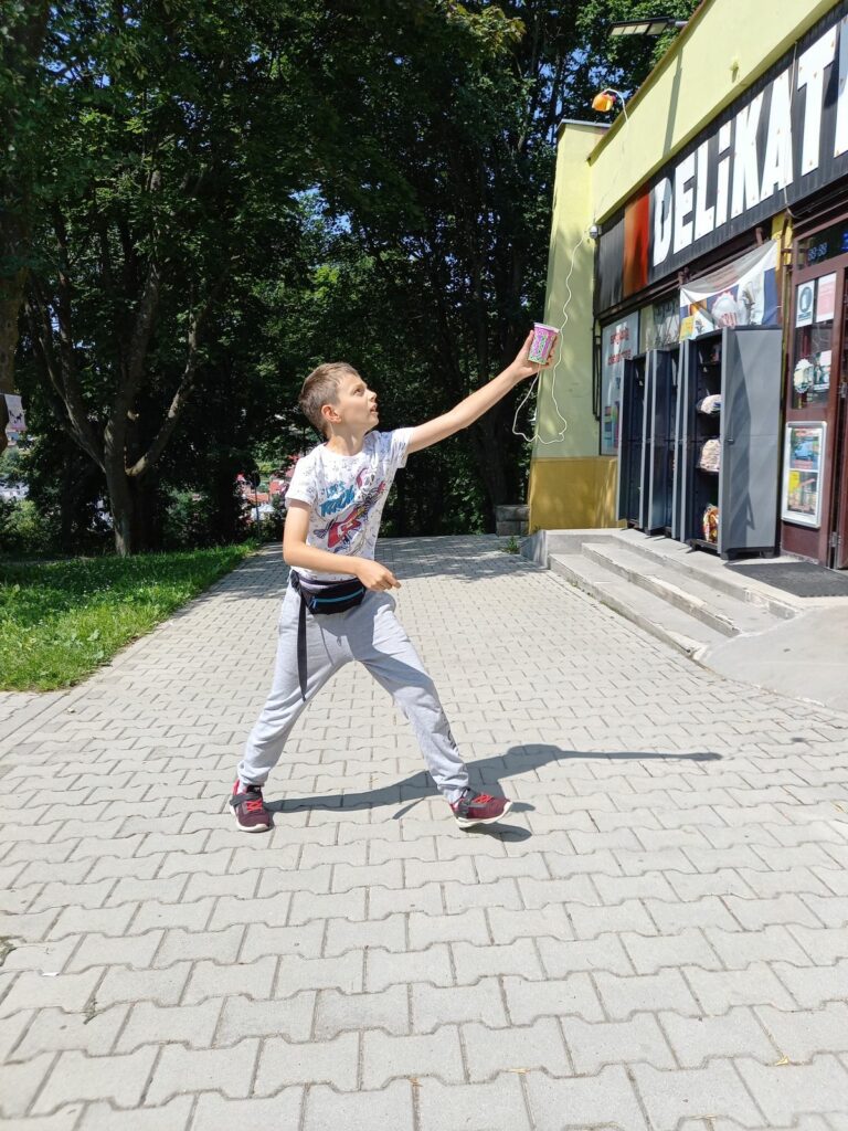 Na zdjęciu chłopiec w wieku szkolnym podskakuje z plastikowym kubkiem
