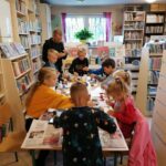 Biorąca udział w „Eko- Warsztatach” grupa dzieci oraz pan bibliotekarz malują w skupieniu kamyki zamieniając je w różne zwierzątka.