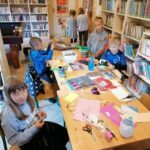 Grupa kilku dziewczynek i chłopców pracuje w skupieniu przy bibliotecznym stole ozdabiając swoje Eko- doniczki.