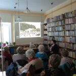 Pani dyrektor biblioteki przedstawia wyświetlane kolejne ilustracje kuracjuszom siedzącym w sali czytelni