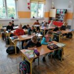Uczniowie siedzą w ławkach i w skupieniu rysują na kartkach portret starego górala Zwyrtały.