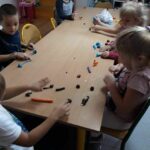 Grupa dzieci siedzi przy stole i przy pomocy plasteliny i kasztanów „buduje” kolorowe ślimaki.