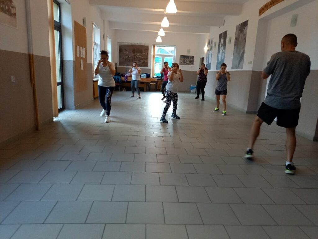 Na zdjęciu widać 6 uczestniczek projektu "MAMY-to!" w strojach sportowych oraz trenera podczas wykonywania ćwiczeń fizycznych.