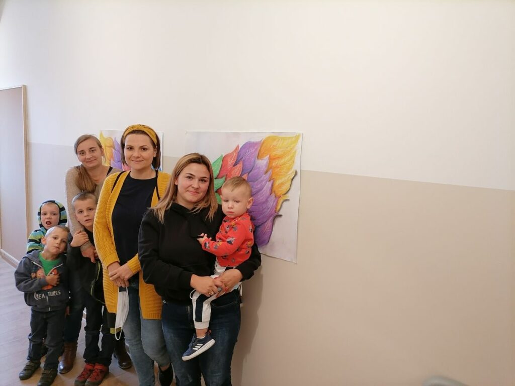 Na zdjęciu widać 3 uczestniczki projektu "MAMY-to!" wraz z dziećmi (czterech chłopców) pozujących na tle wielobarwnych skrzydeł.