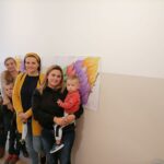 Na zdjęciu widać 3 uczestniczki projektu "MAMY-to!" wraz z dziećmi (czterech chłopców) pozujących na tle wielobarwnych skrzydeł.