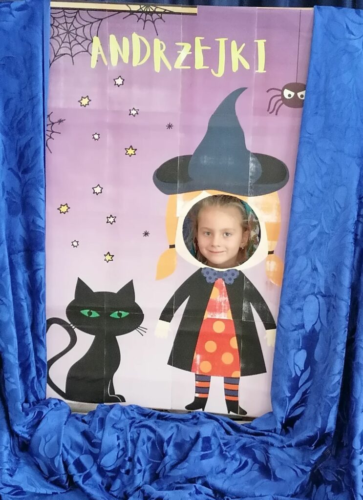 Na zdjęciu widoczna jest dziewczynka pozująca do zdjęcia w foto-budce z czarownicą.