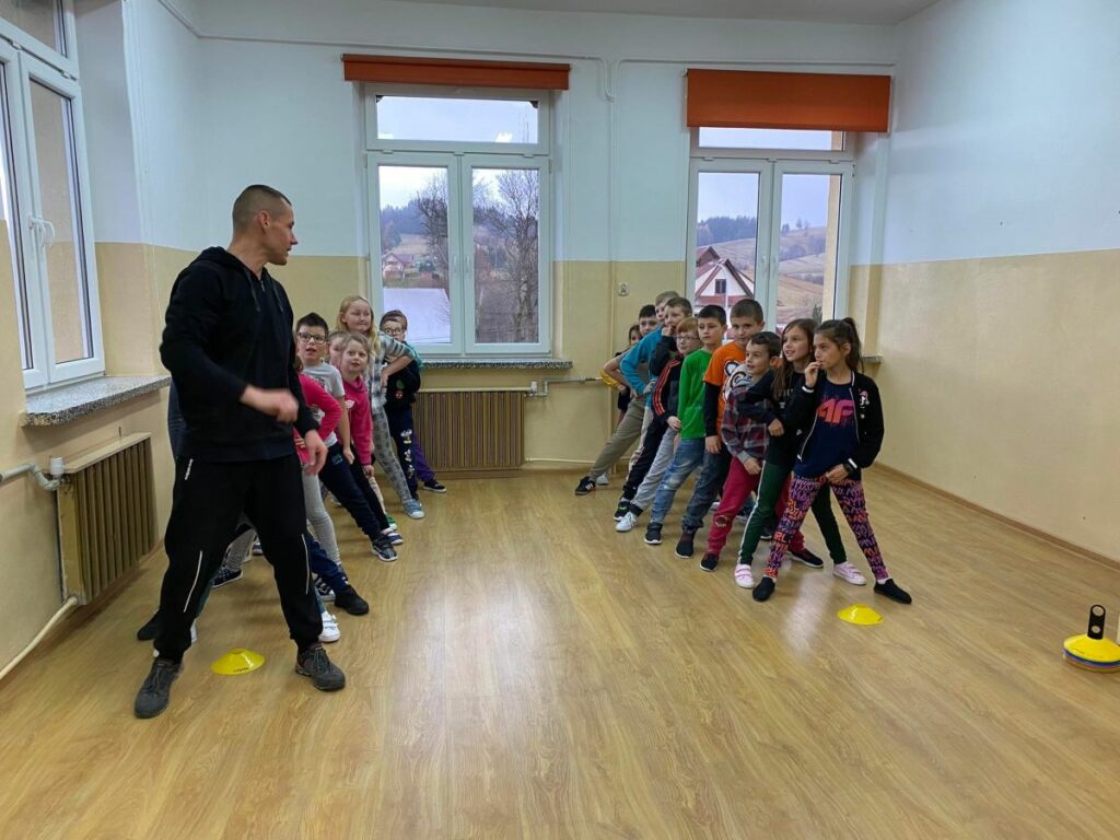 Grupa dzieci stoi podzielona na dwie drużyny w szerokich rozkrokach. Za chwilę zaczną się „wyścigi w tunelach” i zabawa „sałatka jarzynowa”.