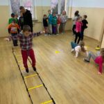 Mali sportowcy są ustawieni w kolejce w jednym końcu sali, przed nimi znajduje się ułożony z drabinki koordynacyjnej i stożków sprawnościowy tor przeszkód, który każdy musi pokonać.