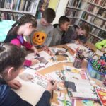Na fotografii widać dzieci które siedzą wokół stołu wykonując kolorowe prace plastyczne. Stół zapełniony jest różnego rodzaju materiałami plastycznymi.