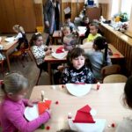 na zdjęciu widać dzieci siedzące przy stolikach i wykonujące prace plastyczną.