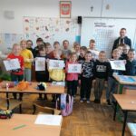 Pamiątkowe zdjęcie dzieci z klasy pierwszej i drugiej oraz stojącego razem z nimi pana bibliotekarza. Każdy z uśmiechniętych uczniów trzyma w rękach wykonany przez siebie górniczy rysunek.