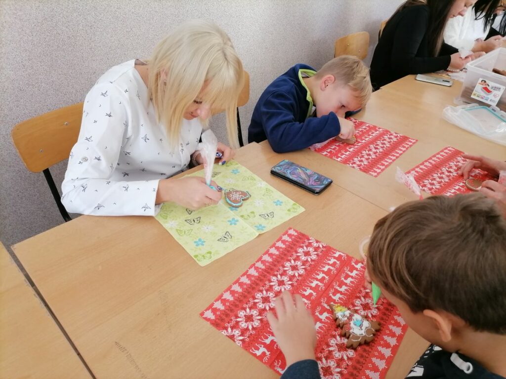 Na zdjęciu widoczna jest kobieta oraz dwoje dzieci podczas dekorowania pierniczków.